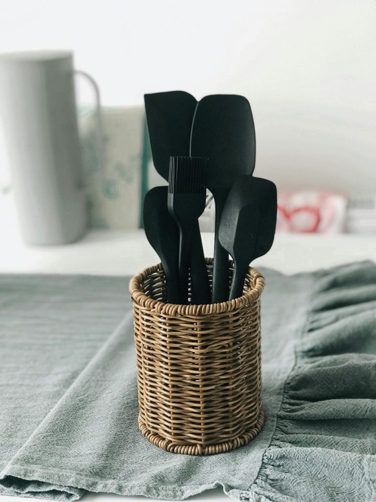 Black kitchen utensils in a wicker basket on a kitchen counter.