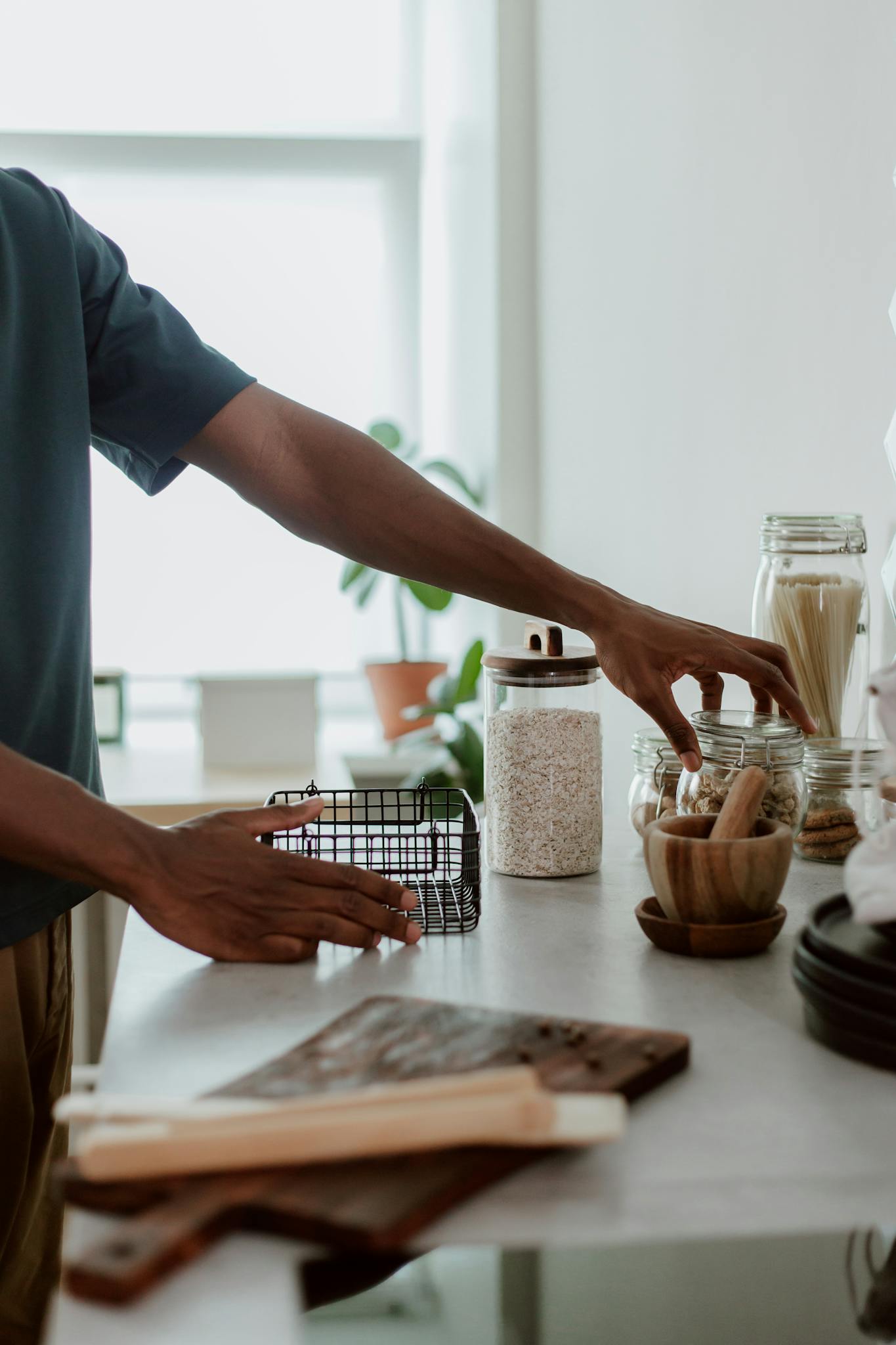 Close-up of hands arranging glass jars and utensils on a kitchen countertop.